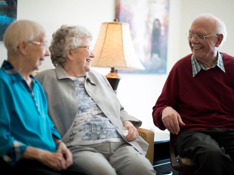 A man and two women have a pleasant conversation in a social area of the assisted living facility.
