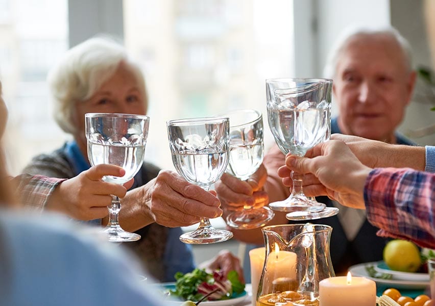 Senior residents celebrate being hydrated by all clicking their drinking glasses together across a shared dining table.