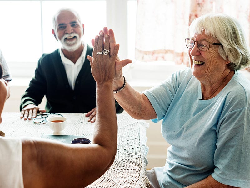 Friendship is exemplified by a cheerfull high five among two residents as another resident watches from across the table.