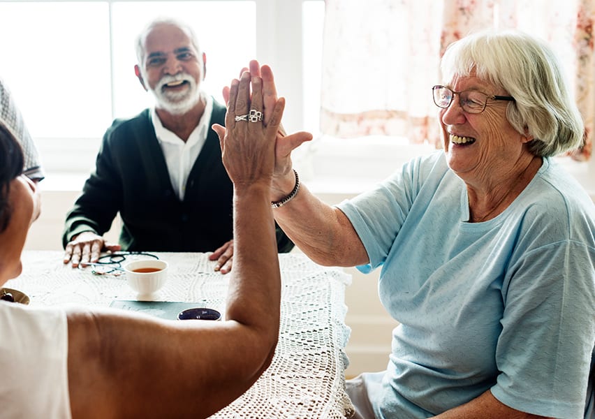 Friendship is exemplified by a cheerfull high five among two residents as another resident watches from across the table.