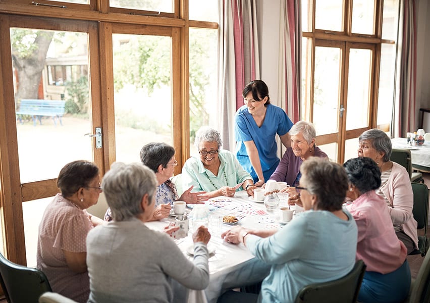 Women in an assisted living community gather around a table for a fun game of cards.