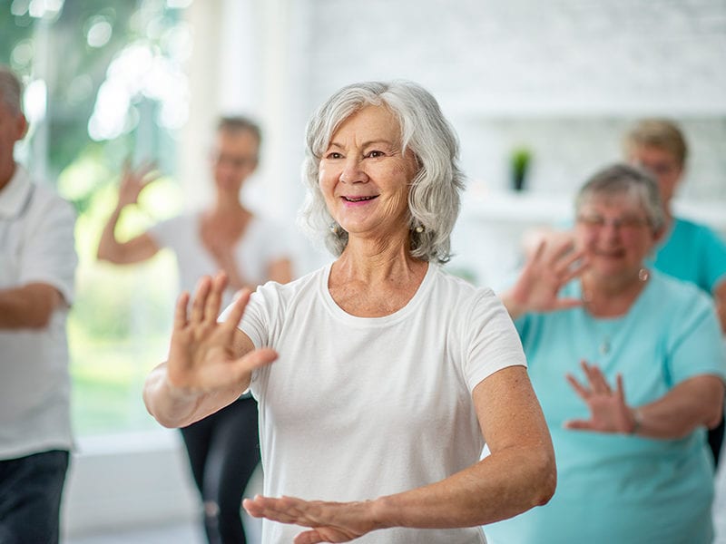 A senior Culpepper Place woman resident is doing low impact movements among friends in an exercise class.