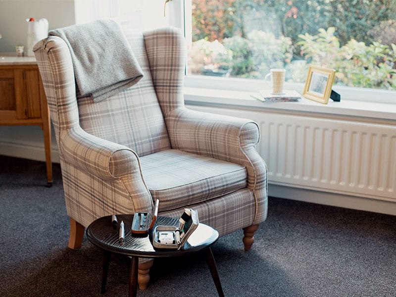 A gray armchair sits by a window in an assisted living facility