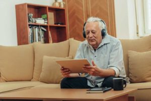Man sitting on a sofa listening to podcasts for seniors on an iPad