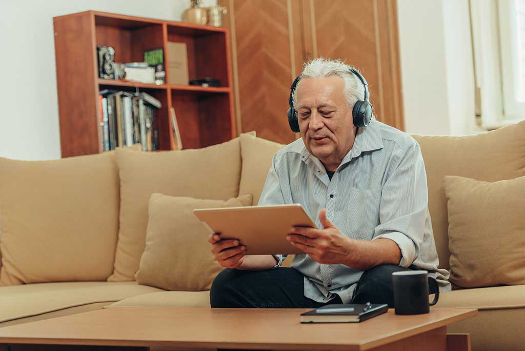 Man sitting on a sofa listening to podcasts for seniors on an iPad