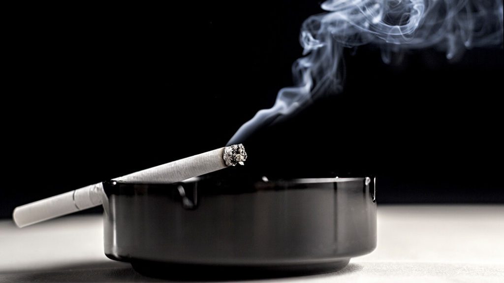 A cigarette smolders in an ashtray representing the health risks of smoking over age 50